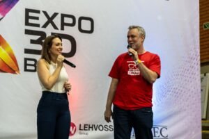 Apresentadores no palco principal da Expo3DBR 2026 com o logotipo do evento ao fundo.